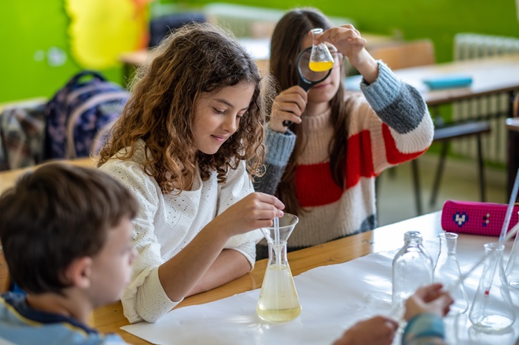 teenagers at school learning about chemistry, mixing chemicals, sitting on benches together, in the classroom, laughing, studying, researching, reading, microscope