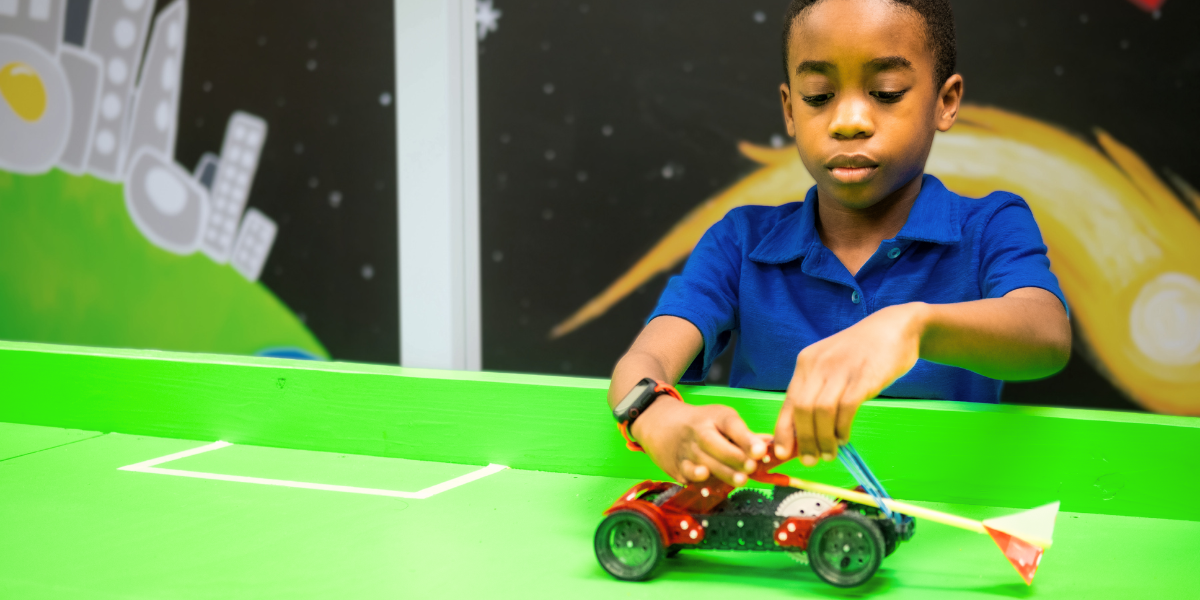 Young student assembling a motorized vehicle at an Engineering For Kids<sup srcset=