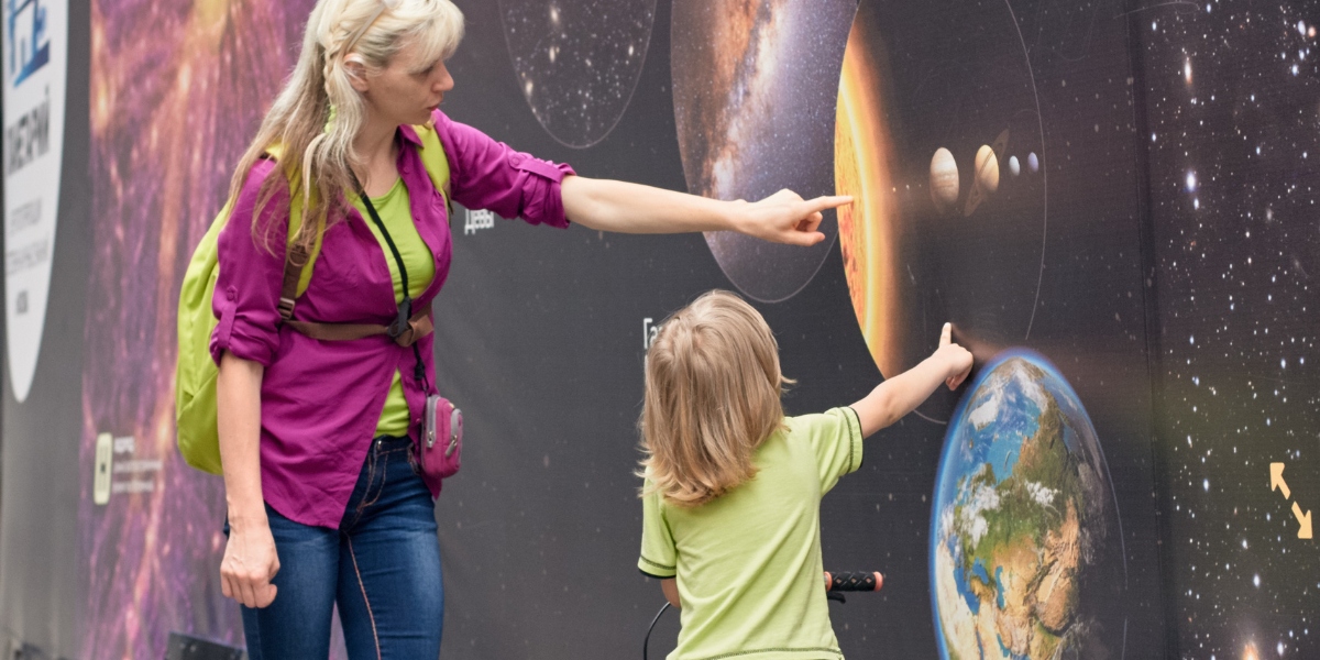Mother and child getting excited about space at a planetarium, pointing at planets on an interactive solar system display wall exhibit, perfect for hands-on learning.