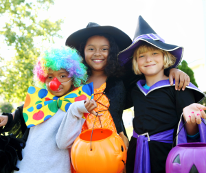 Three children in Halloween costumes including clown, witch, and wizard holding trick-or-treat buckets while learning STEM concepts 